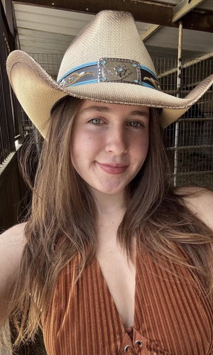 Woman with long brown hair wearing cowboy hat and brown top indoors.