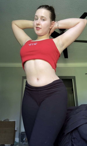 Woman in red crop top and black leggings posing indoors.