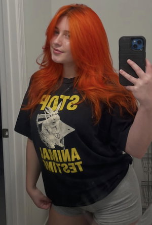 Woman with orange hair in black t-shirt taking mirror selfie indoors.