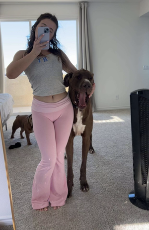 Woman in gray tank top and pink pants taking mirror selfie with dog.