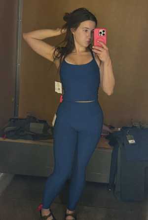 Woman in blue activewear taking mirror selfie indoors.