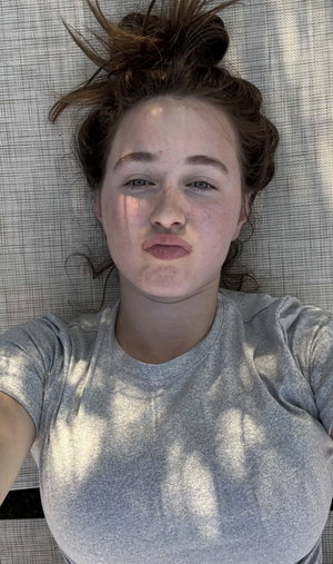 Woman with freckles and messy bun lying on textured surface, wearing gray t-shirt.