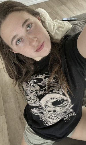Woman with long brown hair in black t-shirt taking indoor selfie.
