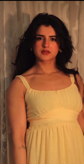 Woman with long dark hair wearing yellow dress indoors.