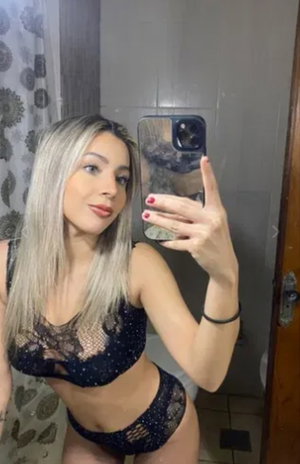 Blonde woman in black lace lingerie taking bathroom mirror selfie.