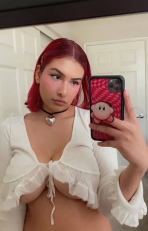 Red-haired woman in white top takes mirror selfie indoors.