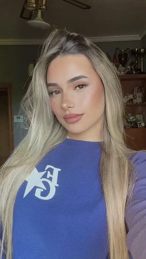 Blonde woman in blue sweater taking indoor selfie.