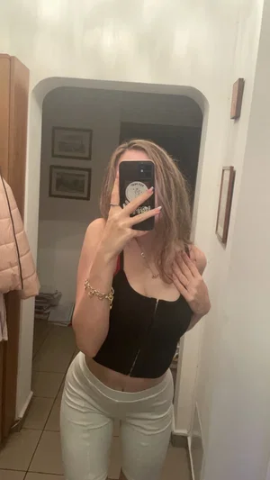 Woman in black crop top and white pants taking mirror selfie in hallway.