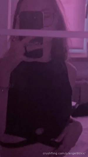 Woman in black top taking mirror selfie in dimly lit room.