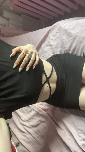 Woman in black strappy top lying on pink bed, hand on hip.