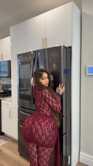 Curvy woman in red lace bodysuit in kitchen.