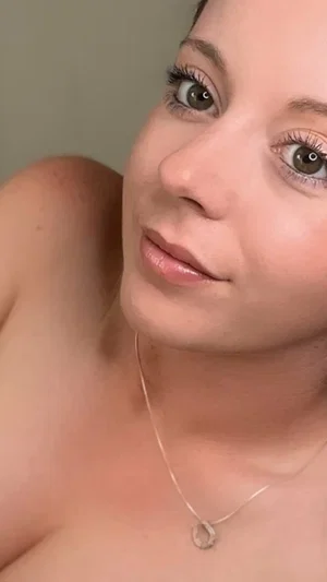 Woman with bare shoulders and necklace, close-up selfie indoors.