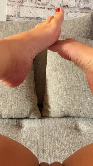 Close-up of bare feet with red toenails resting on gray couch cushions.