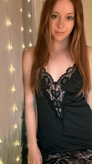 Redhead in black lace lingerie in bedroom with fairy lights.