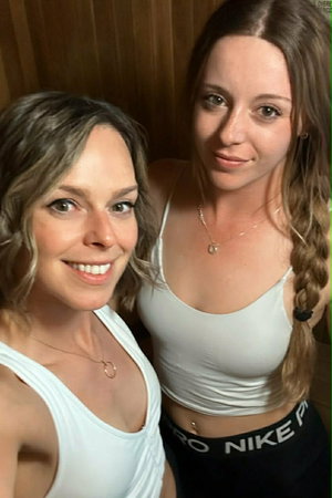 Two women in white tank tops taking a selfie indoors.