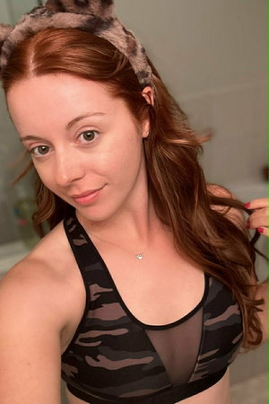 Woman with red hair wearing camo sports bra and furry headband, indoors.