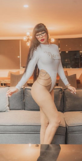 Woman in white long-sleeve bodysuit with cutout, posing in living room with sofa.