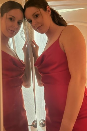 Woman in red dress taking mirror selfie in bathroom.