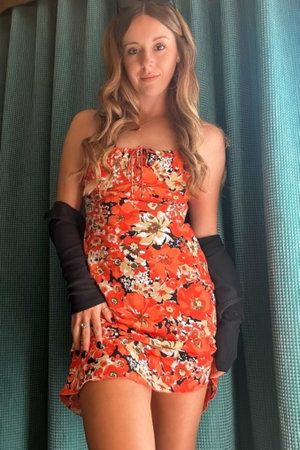 Woman in floral dress and black gloves posing in front of teal curtains.
