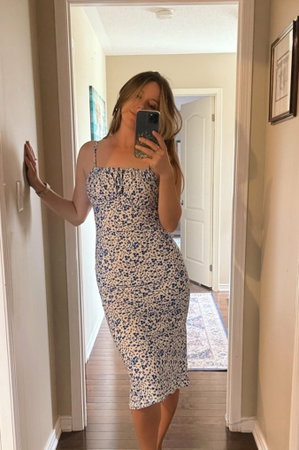 Woman in floral dress taking mirror selfie in hallway.