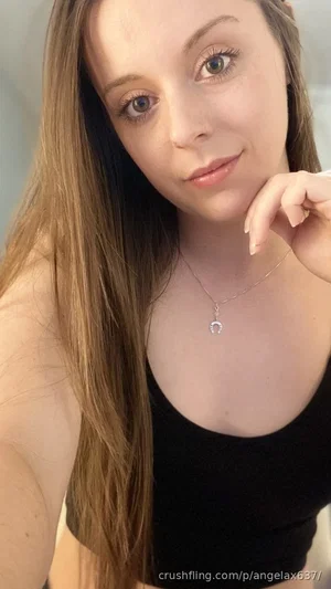 Woman with long brown hair wearing black crop top, indoors, posing for selfie.