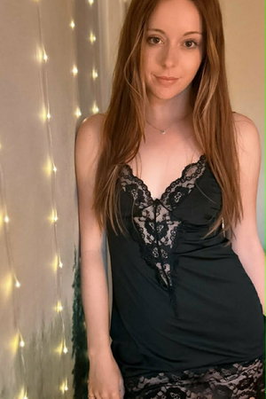 Woman with long auburn hair in black lace dress indoors.