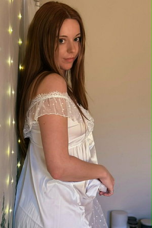 Woman with long brown hair in white dress indoors by lights.