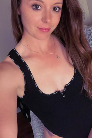 Woman with long brown hair wearing black tank top with white text, indoors.