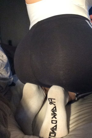 Person in black shorts and white top on bed with socks.