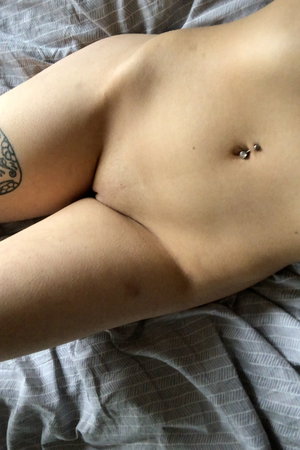 Person with navel piercing and arm tattoo lying on bed.