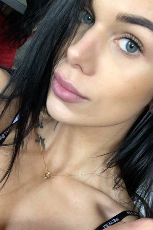 Woman with long black hair and tattoos wearing black lingerie.