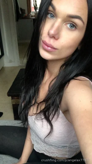 Woman with long black hair in a light lace top, sitting indoors.
