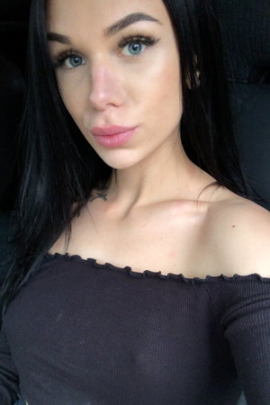 Woman with long black hair wearing black off-shoulder top in car.