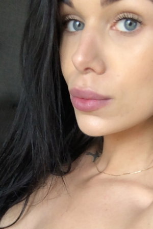 Woman with long black hair and blue eyes taking a close-up selfie.