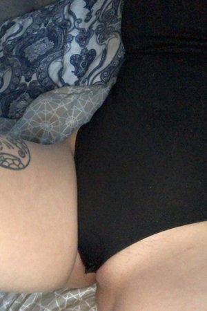 Person with tattooed arm wearing black shorts, lying on patterned bedding.