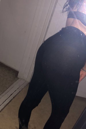 Woman in black leggings and top, standing indoors near door, back view.