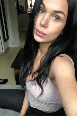 Dark-haired woman in lace top taking indoor selfie.