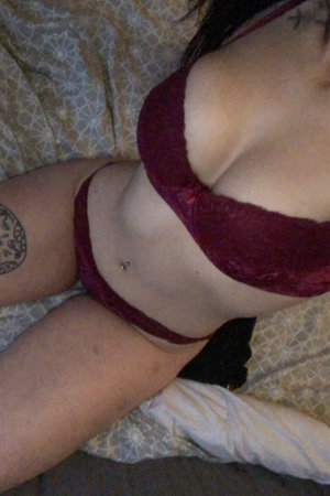 Woman in maroon lace lingerie on bed with tattoos.