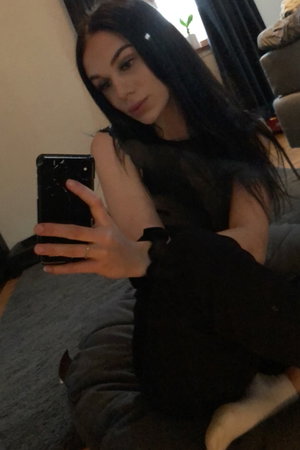Woman with long dark hair taking a selfie indoors in black top.