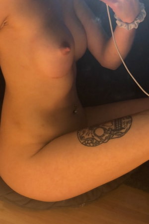Woman with tattoo on thigh, bare chest, sitting indoors.