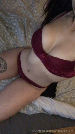 Woman in maroon lingerie lying on patterned bedspread, tattoo on thigh.