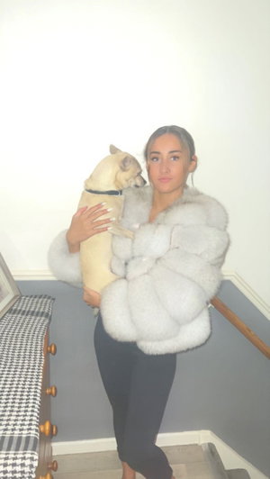 Woman in fur coat holding dog on indoor stairs.