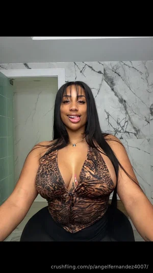 Woman with long black hair in leopard print top and black bottoms, posing in a bathroom with marble
