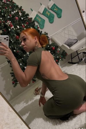 Woman with red hair in green backless dress kneeling by Christmas tree in bedroom.