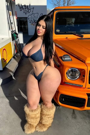 Woman in blue bikini and fur boots posing by orange truck at gas station.