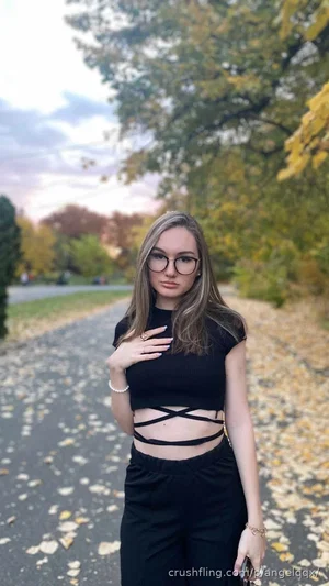 Woman in black crop top and pants standing on leafy path outdoors.