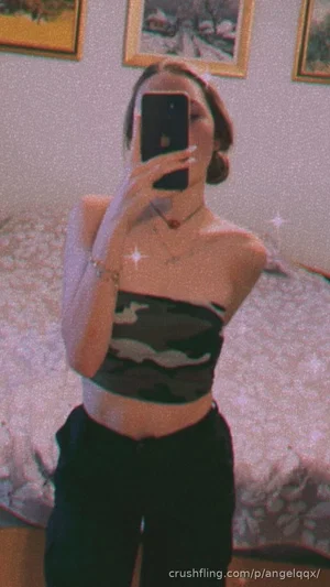 Woman in camo crop top and black pants takes mirror selfie in bedroom.