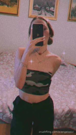 Woman in camo crop top and black pants takes mirror selfie in bedroom.