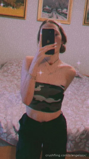 Woman in camo crop top and black pants takes mirror selfie in bedroom.