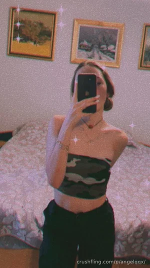 Woman in camo crop top and black pants takes mirror selfie in bedroom.
